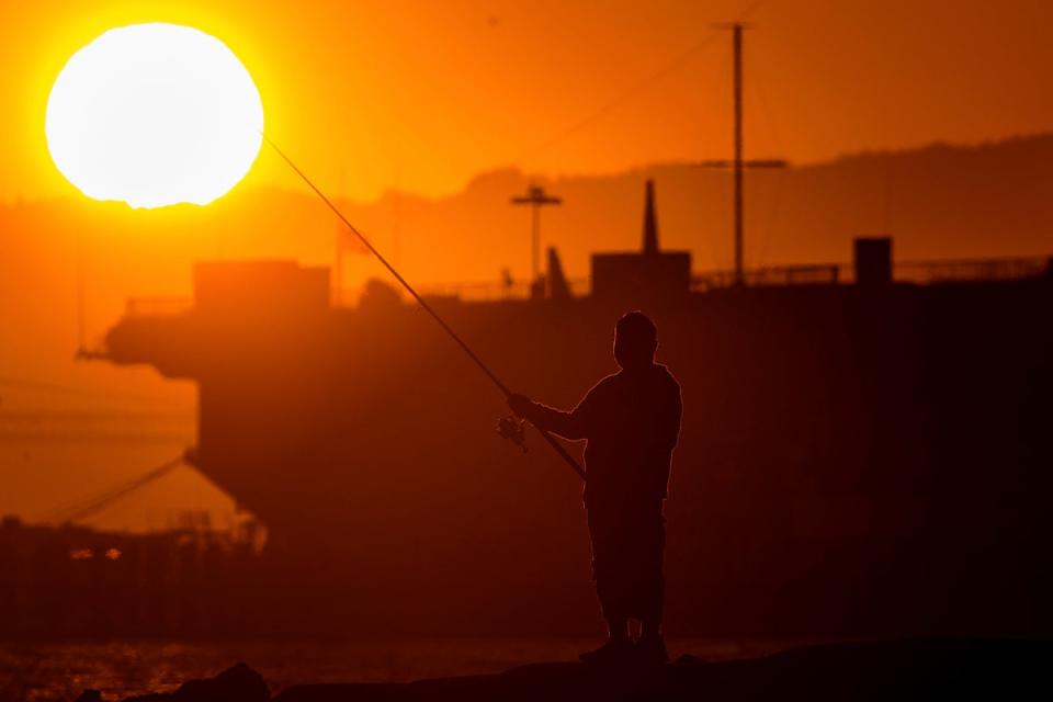 A man fishes off a jetty in Alameda, California, as the sun sets over the San Francisco Bay on July 1. An extended heatwave predicted to blanket Northern California has resulted in red flag fire warnings and the possibility of power shutoffs beginning Tuesday