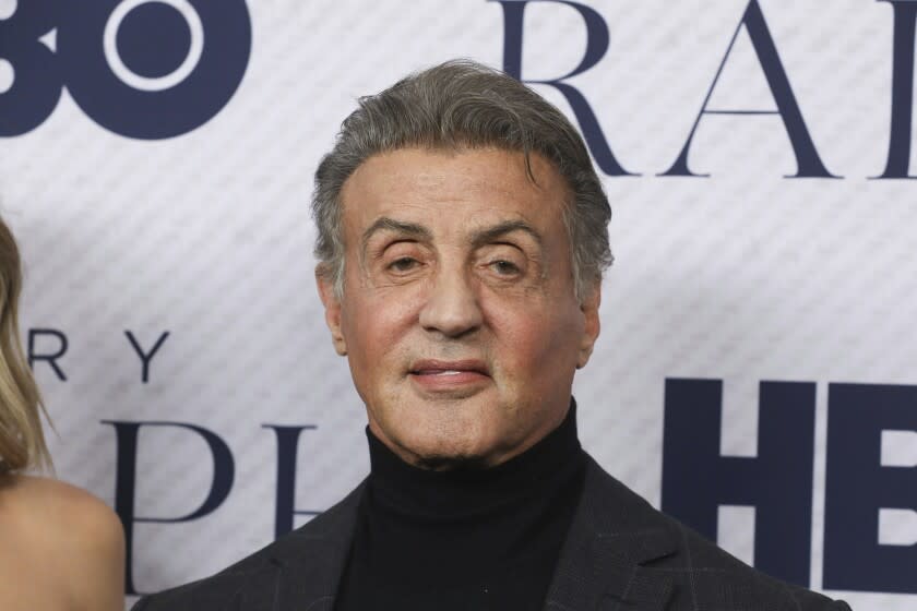 An older man wears a black turtleneck and gray blazer