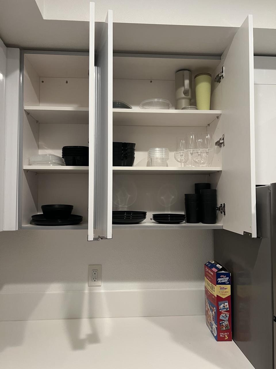 Open kitchen cabinet with neatly arranged black and white dishes, cups and stacked plates and bowls