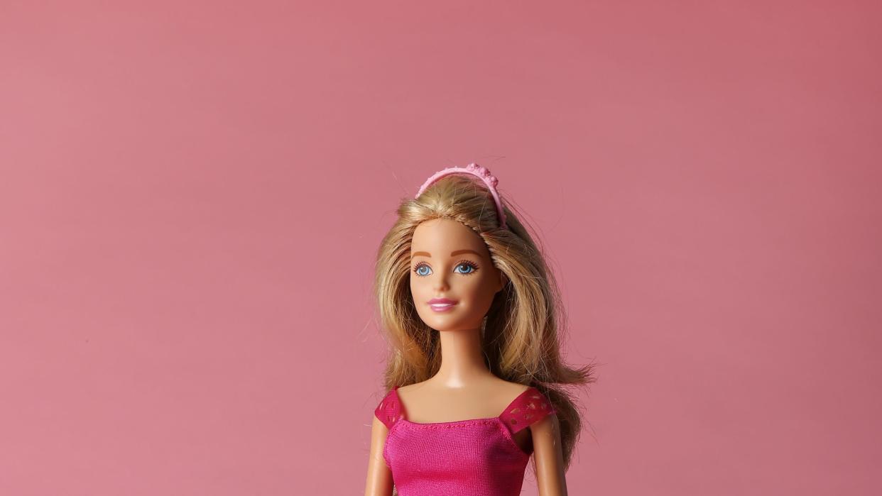 a blonde barbie doll wears a pink dress with a black belt and a pink headband