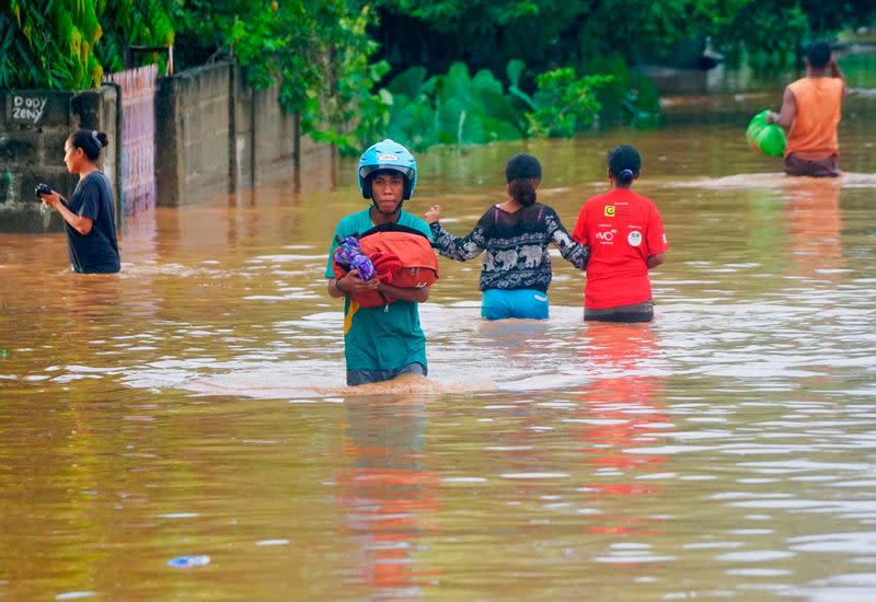 A man wearing a helmet carries his goods through the water in an area affected by floods after heavy rains in Dili