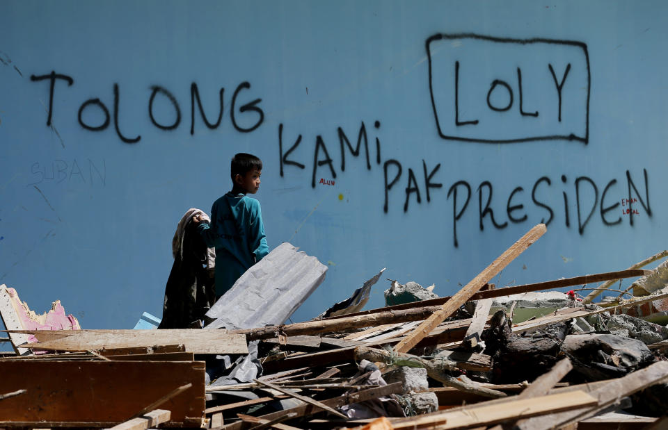 A child takes an item in front of a wall with the writing which reads " Help us Mr. President " amidst destruction caused by the massive earthquake and tsunami in Loly, Central Sulawesi, Indonesia Friday, Oct. 5, 2018. French rescuers say they've been unable to find the possible sign of life they detected a day earlier under the rubble of a hotel that collapsed in the earthquake a week ago on Indonesia's Sulawesi island. (AP Photo/Tatan Syuflana)