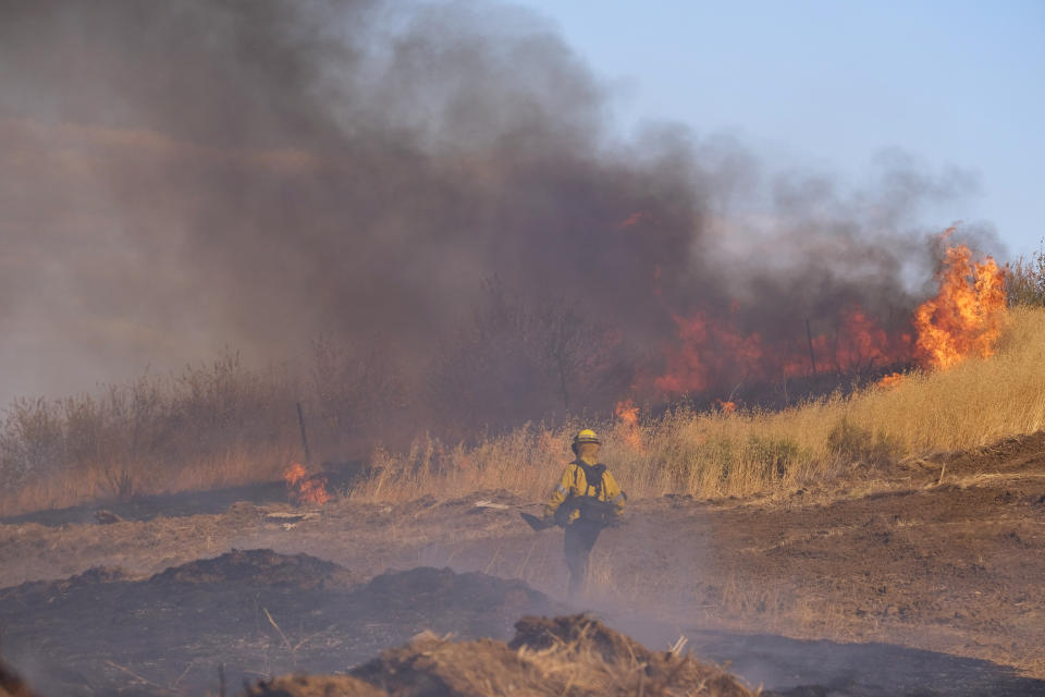 Un bombero camina entre un incendio en la ladera de una colina, el miércoles 31 de agosto de 2022, en Castaic, California. (AP Foto/Ringo H.W. Chiu)