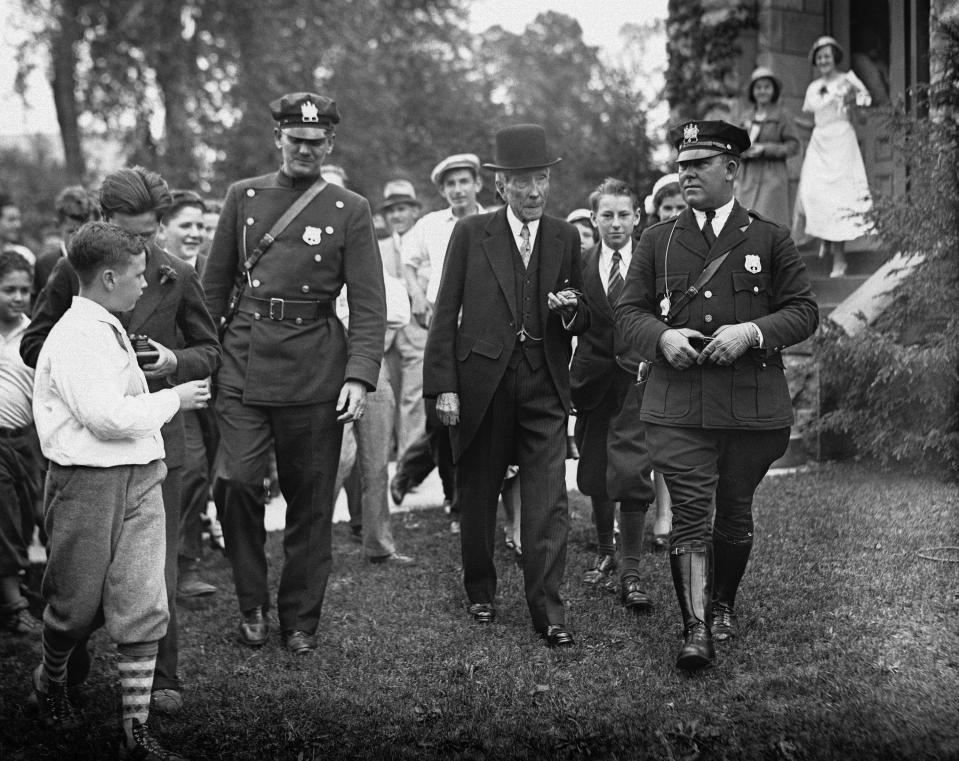 FILE - In this May 14, 1933 file photo, John D. Rockefeller, Sr. is surrounded by state troopers and admirers as he attended church in Lakewood, N.J. In the early 21st century, members of the economic elite are looking for ways to reduce the nation's growing income inequality for a variety of reasons, from self-interest to pangs of conscience. "Names like Carnegie, Mellon and Rockefeller_ the (Warren) Buffet and (Bill) Gates of their days - grace universities, museums and medical centers in part because the originators of those fortunes gave back," Harvard Business School professor Michael Norton says. (AP Photo, File)