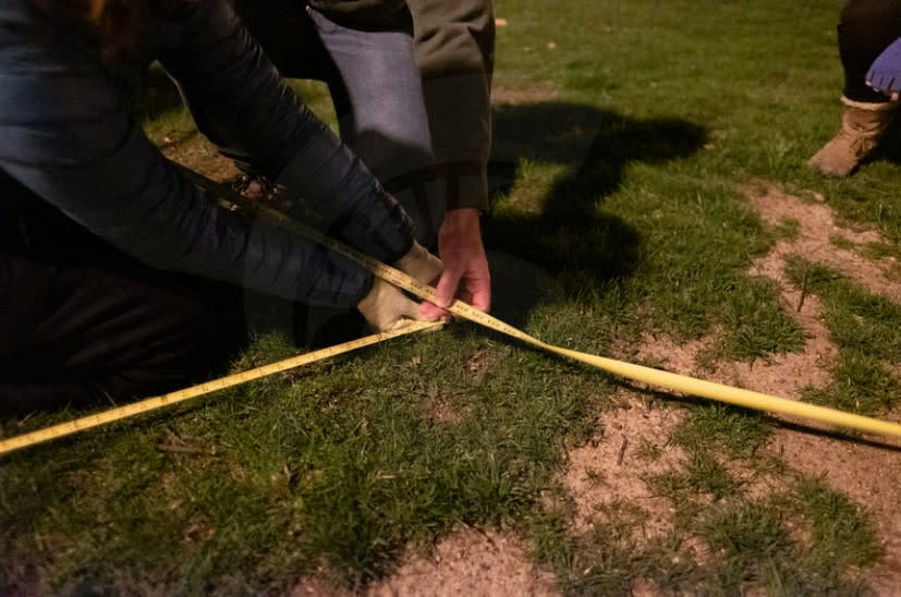 Two people use yellow measuring tapes to create an "X" and find the exact location of their target.