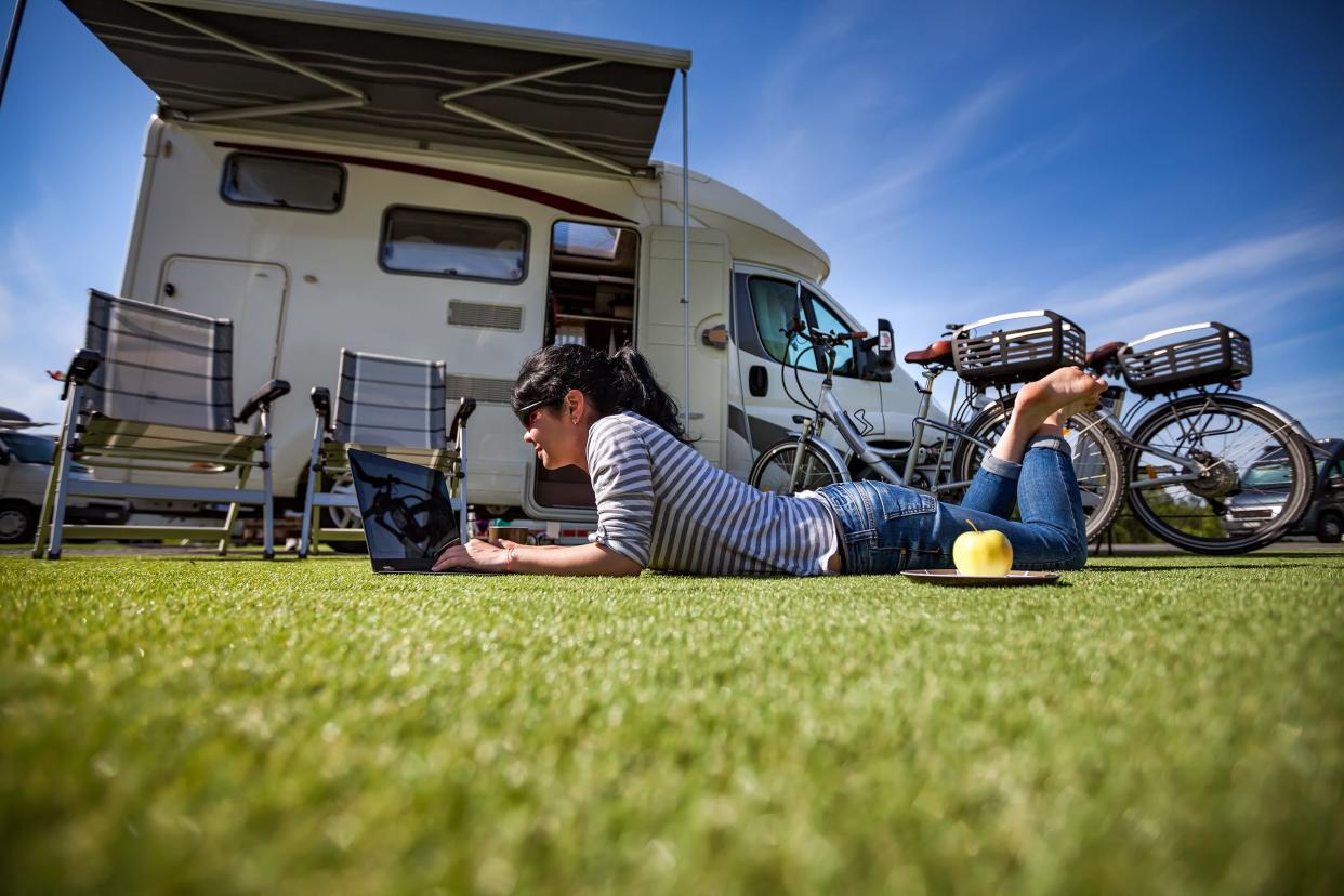 woman on grass with laptop, rv in the background