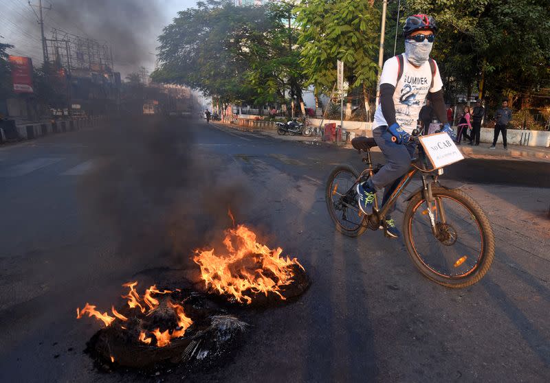 A cyclist passes burning tyres set ablaze by protesters during the strike called by AACSU to protest against the bill in Guwahati