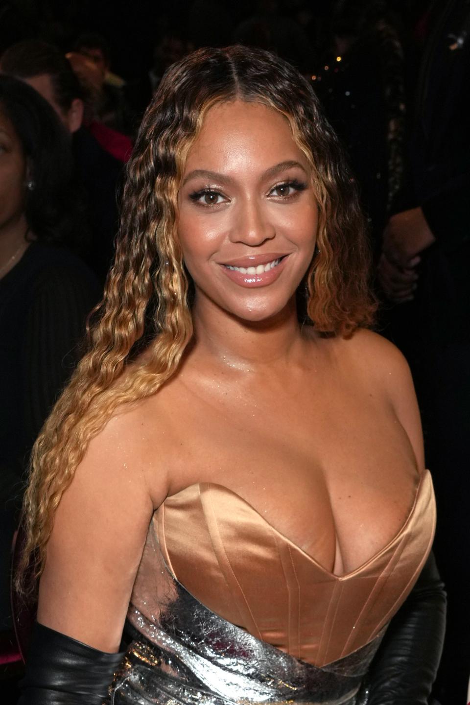 Beyoncé seated at an event wearing a metallic gown with a structured, strapless bodice