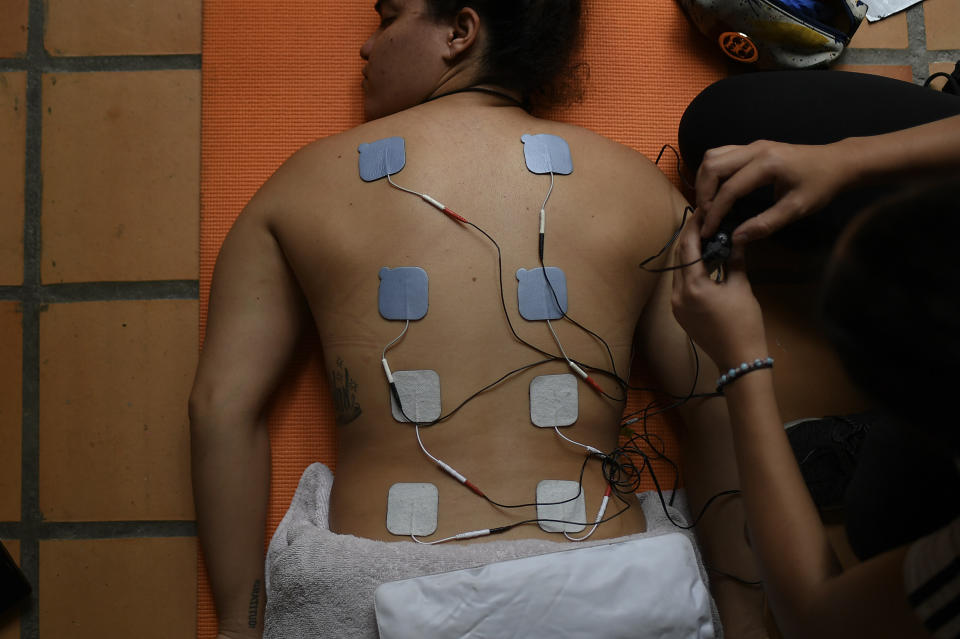 La venezolana Stefany Hernández, medallista olímpica en BMX, recibe electroestimulación en la espalda por parte de su fisioterapista en Caracas, el lunes 25 de mayo de 2020 (AP Foto/Matías Delacroix)