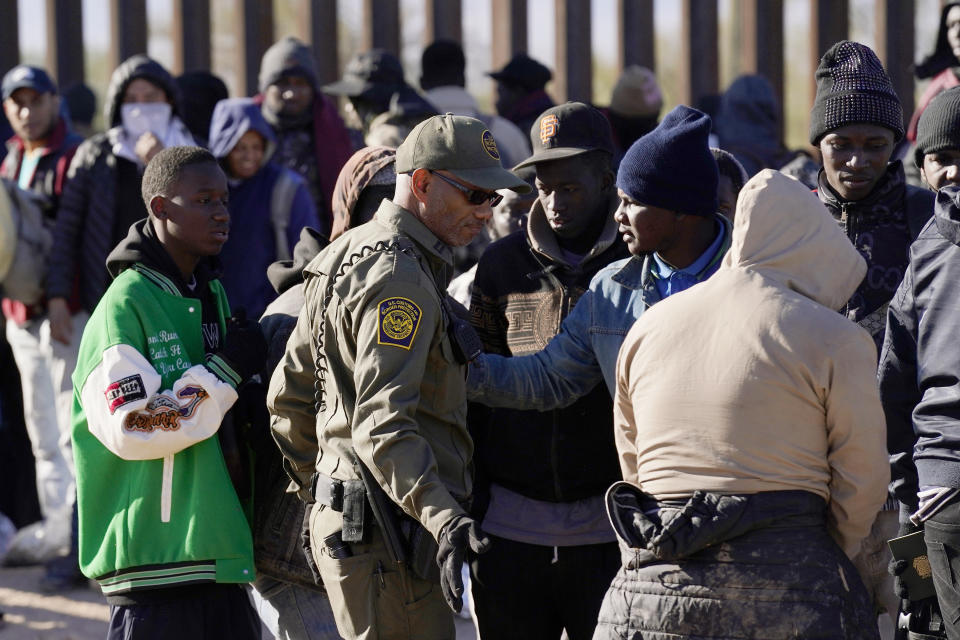 A member of U.S. Customs and Border Protection tries to control a group of migrants as hundreds gather along the border after breaking through gaps in the border wall Tuesday, Dec. 5, 2023, in Lukeville, Ariz. The U.S. Border Patrol says it is overwhelmed by a shift in human smuggling routes, with hundreds of migrants from faraway countries like Senegal, Bangladesh and China being dropped in the remote desert area in Arizona. (AP Photo/Ross D. Franklin)