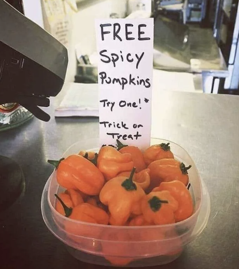Sign reads "FREE Spicy Pumpkins Try One! Trick or Treat" with a bowl of small orange peppers shaped like pumpkins