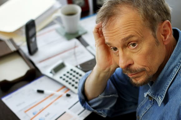 A visibly worried man resting his head on his hand, with bills on the desk in front of him.