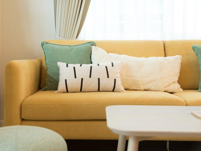 A large yellow couch with white and green pillows fills living room