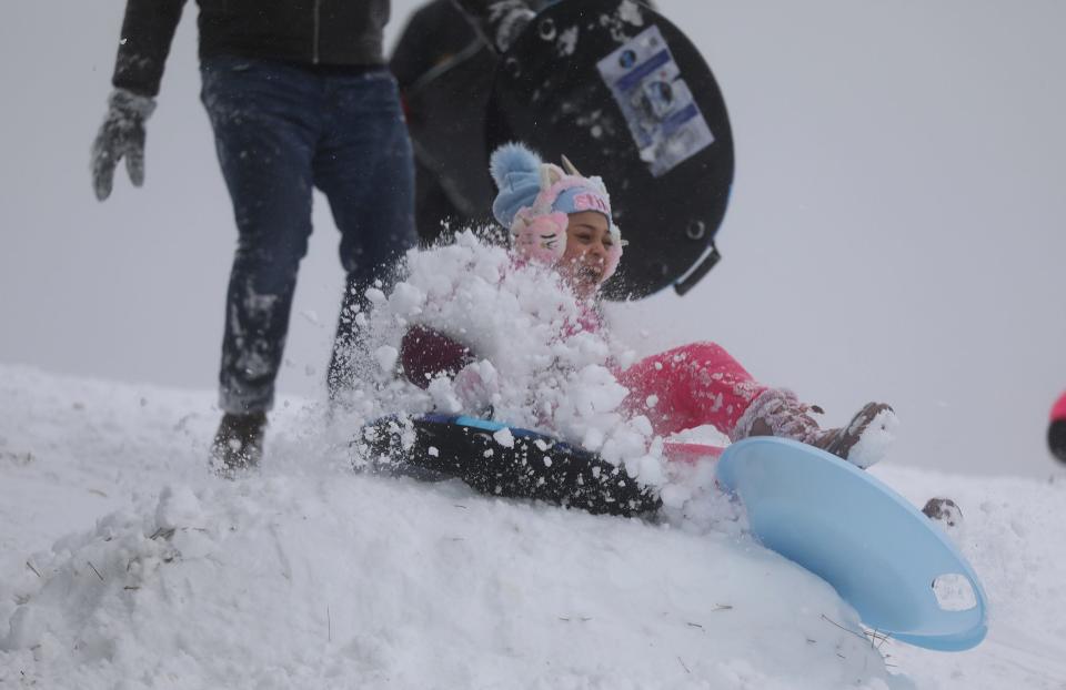 Lydialy Santiago, 9, of Rochester, New York, laughs as she hits a mogul and gets sprayed with snow after a push from her father, Reynnier Santiago, while sledding on a hill near Cobbs Hill Reservoir in Rochester, Sunday, Jan. 7, 2024.