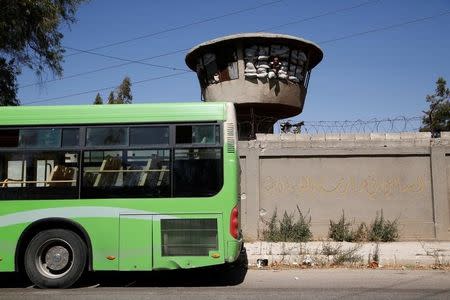 A Syrian Army soldier looks out of a look out point near a bus that was supposed to evacuate people near the entrance of the Waer district in the central Syrian city of Homs, Syria September 19, 2016. The text on the wall reads in Arabic, "Essential in the practice of democracy". REUTERS/Omar Sanadiki