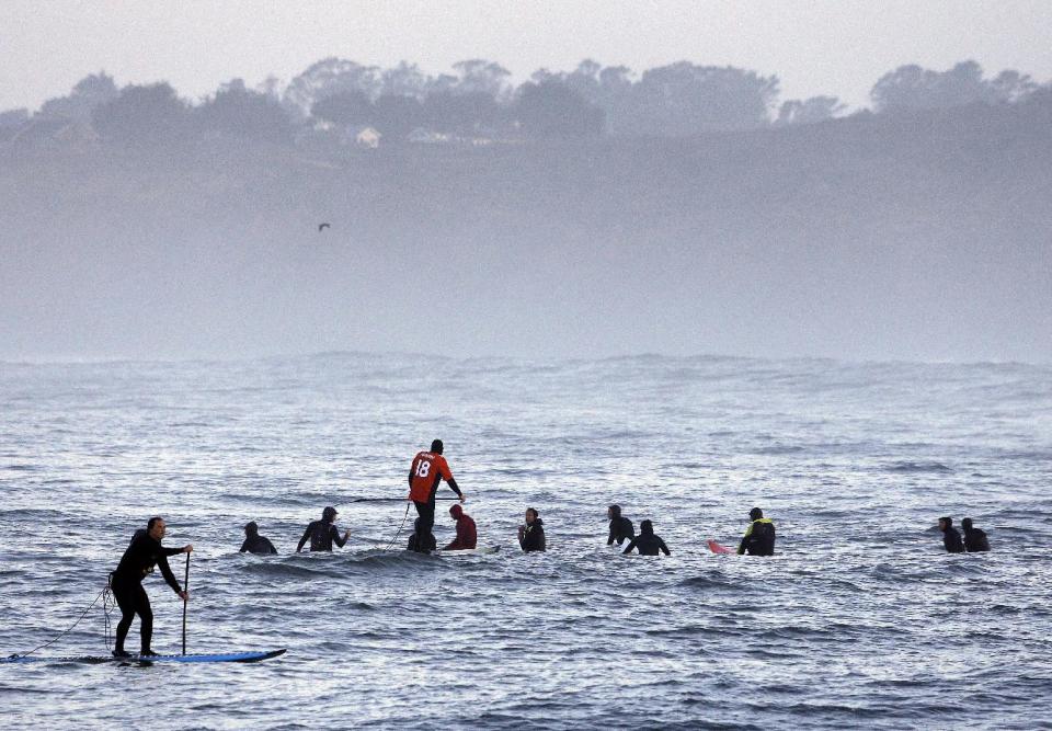A man paddleboards, left, past a group of surfers waiting to catch a wave in the first heat of the first round of the Mavericks Invitational big wave surf contest Friday, Jan. 24, 2014, in Half Moon Bay, Calif. (AP Photo/Eric Risberg)