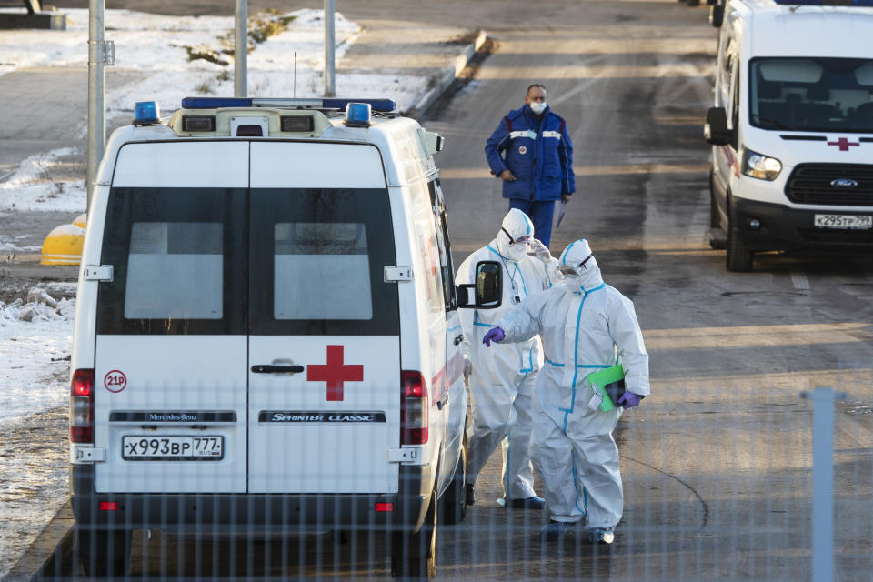 Medical workers wearing protective gear return to their ambulance after transferring a patient suspected of having coronavirus at a hospital in Kommunarka, outside Moscow, Russia, Saturday, Dec. 5, 2020. Thousands of doctors, teachers and others in high-risk groups have signed up for a COVID-19 vaccination in Moscow starting Saturday, a precursor to a Russia-wide immunization effort. (AP Photo/Pavel Golovkin)