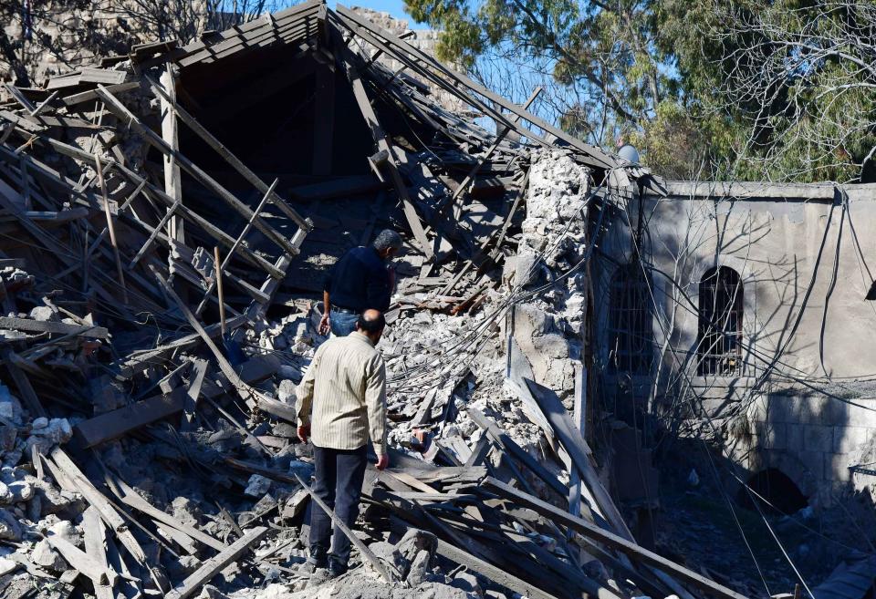 A middle-aged man, seen from behind, peers into a pile of debris from a shattered building after an Israeli missile attack.