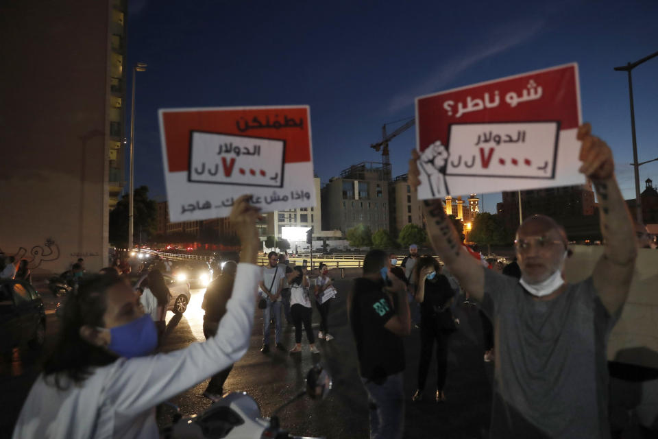 Anti-government protesters carry placards in Arabic that read, "What are you waiting for, 1$ = 7000 Lebanese pounds," as others block a road during a protest against the political leadership they blame for the economic and financial crisis, in front of the government house in downtown Beirut, Lebanon, Thursday, June 11, 2020. (AP Photo / Hussein Malla)