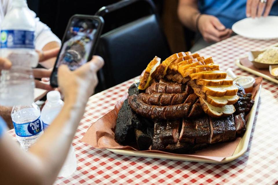 Un cliente toma una fotografía de una bandeja grande de barbacoa repleta de salchichas de Laos, costillas de cerdo, costillas de res y pan de molde recién horneado en Goldee's Barbecue en Fort Worth el viernes 28 de junio de 2024.