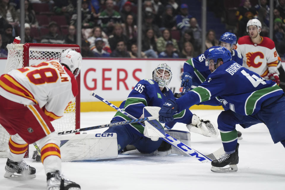 Vancouver Canucks goalie Thatcher Demko (35) stops Calgary Flames' Elias Lindholm (28) as Canucks' Kyle Burroughs (44) defends during the second period of an NHL hockey game Friday, March 31, 2023, in Vancouver, British Columbia. (Darryl Dyck/The Canadian Press via AP)