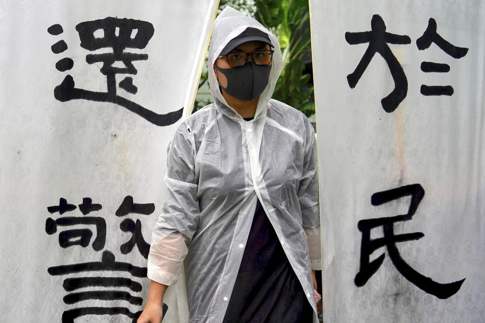 A woman wears a raincoat stands next to banners that read "The duty fulfilled by the police belongs to the people" as people take part in a rally to support the Hong Kong's Police at Edinburgh Place in Hong Kong, Sunday, Aug. 25, 2019. (AP Photo/Vincent Yu)