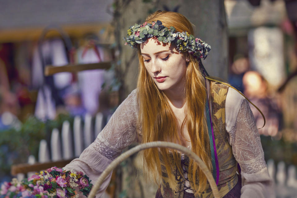 Person dressed in medieval-style attire with a floral crown, holding a basket