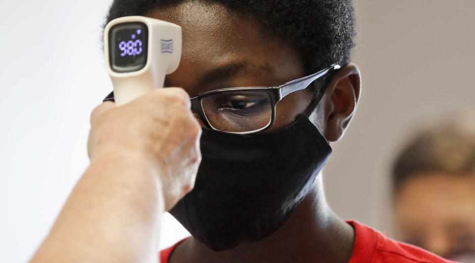 FILE - In this Tuesday, July 14, 2020 file photo, a student wearing a mask has his temperature checked by a teacher before entering a school for summer classes in Texas. On Friday, July 31, 2020, The Associated Press reported on stories circulating online incorrectly asserting that infrared thermometers, which are held near the forehead to scan body temperature without direct contact, point an infrared light directly at the brain’s pineal gland, exposing it to harmful radiation. Infrared thermometers don’t emit radiation into the brain; they sense heat emitted by the body. They pose no risk to the pineal gland, which is located deep within the brain, according to Dr. Haris Sair, director of neuroradiology at Johns Hopkins University. (AP Photo/LM Otero)