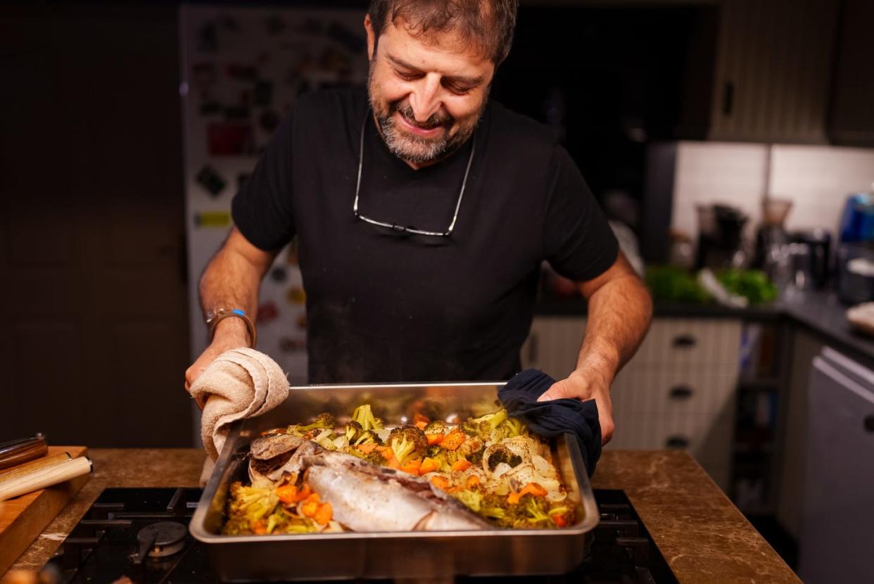 Man holding a hot baking tray with cooked fish