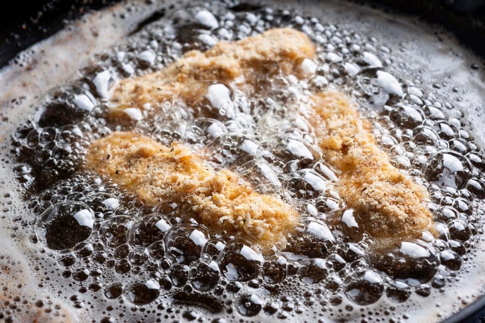 Breaded chicken frying in oil in a pan.