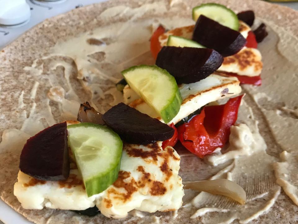 A wholemeal wrap spread with hummus and topped with roasted peppers, halloumi, cucumber, and beetroot.