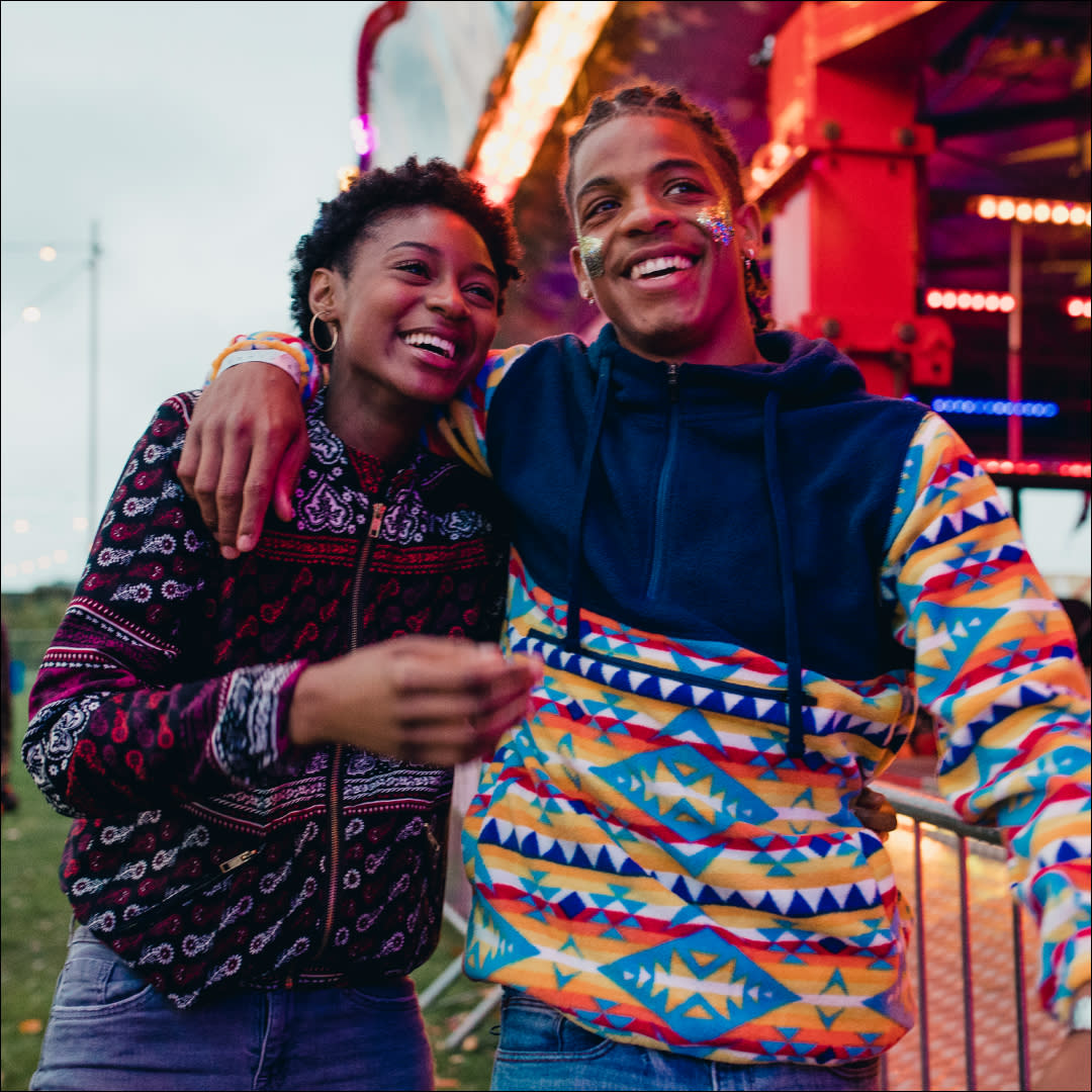 Young couple are laughing and talking as they walk around a funfair on a date. 