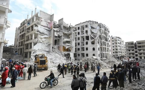 Syrian onlookers gather around rescue teams clearing the rubble in the morning of April 10, 2018 at the site of an explosion in the northwestern city of Idlib.  - Credit: AFP