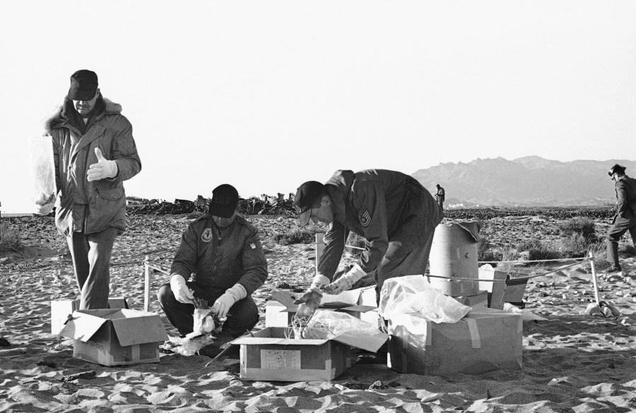 Technicians of the U.S., Air Force use rubber gloves while picking up picking particular pieces of the wreckage and placing them in cardboard boxes in Palomares on Jan. 28, 1966. Main part of the wreckage in background. (AP Photo/Franco Mattioli)