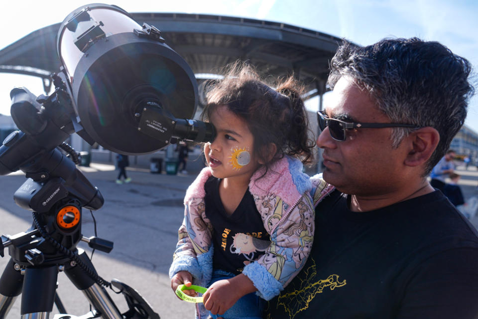 Tawhid Rana, of Midland, Michigan., hold his daughter Thia, as she views the sun through a telescope at the Indianapolis Motor Speedway in Indianapolis, Monday, April 8, 2024.