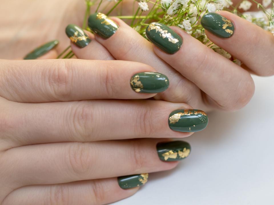 Hands holding flower with green manicure and gold foil on nails.