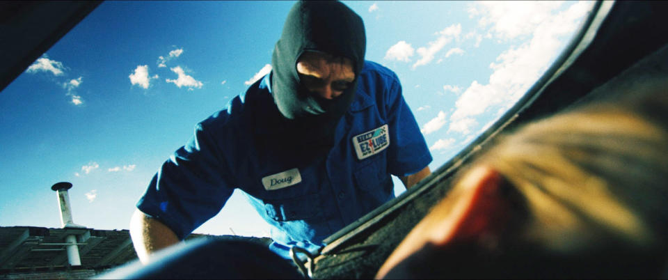 A masked man, labeled "Daniel" on a service uniform, appears to be interacting with someone inside a car trunk on a sunny day