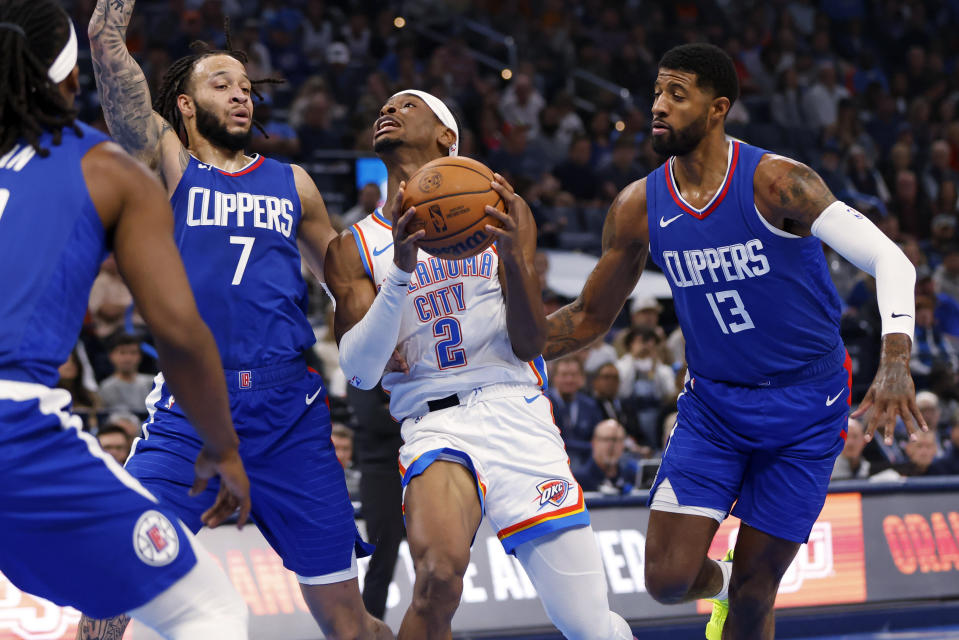 Oklahoma City Thunder guard Shai Gilgeous-Alexander (2) drives to the basket between Los Angeles Clippers guard Amir Coffey (7) and forward Paul George (13) during the first half of an NBA basketball game Thursday, Dec. 21, 2023, in Oklahoma City. (AP Photo/Nate Billings)