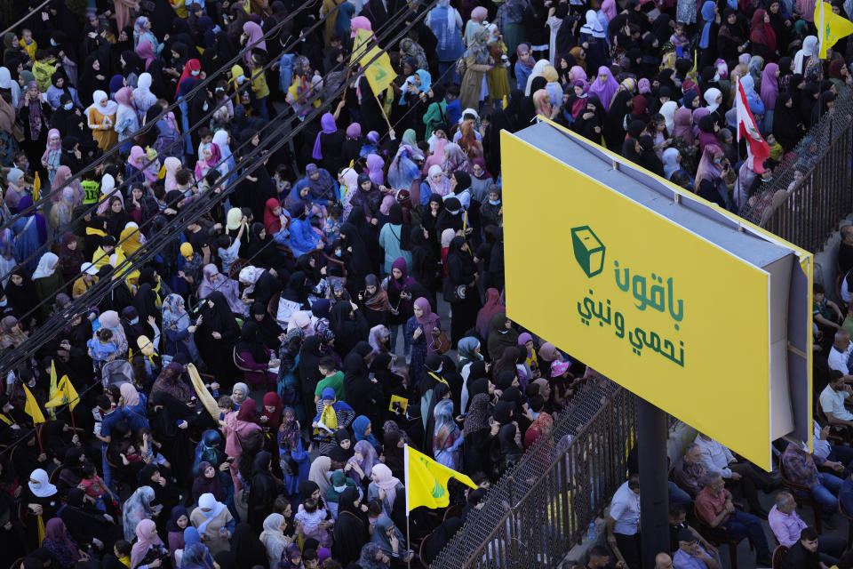 Hezbollah supporters stand under a banner of Hezbollah electoral slogan that read: "We will stay protect and build," during an election campaign, in the southern suburb of Beirut, Lebanon, Tuesday, May 10, 2022. Despite a devastating economic collapse and multiple other crises gripping Lebanon, the culmination of decades of corruption and mismanagement, the deeply divisive issue of Hezbollah's weapons has been at the center of Sunday's vote for a new 128-member parliament. (AP Photo/Hussein Malla)