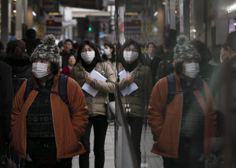 Commuters wearing protective face masks walk on a sidewalk Monday, Jan. 27, 2020, in the Shinjuku district of Tokyo. China has extended its Lunar New Year holiday three more days to discourage people from traveling as it tries to contain the spread of a viral illness that has caused dozens of deaths. (AP Photo/Jae C. Hong)