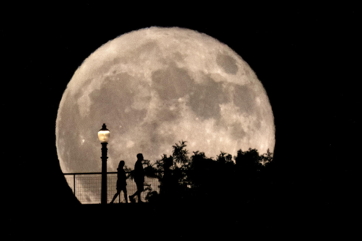 The silhouettes of two people near a lamp post at Griffith Observatory in Los Angeles as the supermoon rises in the night sky. 