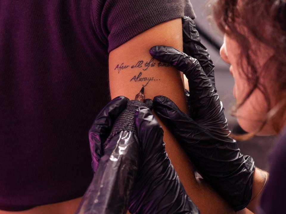 tattoo artists tattooing a harry potter quote on the back of someone's arm