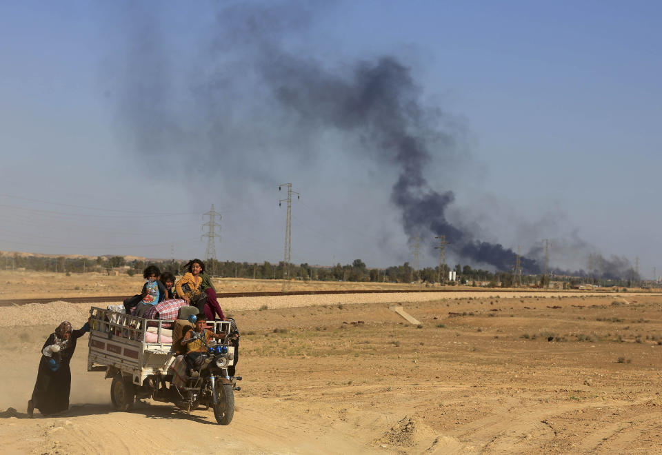 FILE - In this Monday, April 4, 2016 file photo, smoke rises as people flee their homes during clashes between Iraqi security forces and members of the Islamic State group in Hit, Iraq, 85 miles (140 kilometers) west of Baghdad, Iraq.Iraq on Monday, Dec. 10, 2018 celebrated the anniversary of its costly victory over the Islamic State group, which has lost virtually all the territory it once held but still carries out sporadic attacks. (AP Photo/Khalid Mohammed, File)