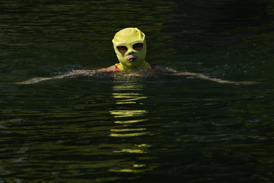 A woman wearing a sun protection headgear and wearing a sun glasses swims to cool off on a sweltering day at an urban waterway in Beijing, Monday, July 10, 2023. Rescuers were looking Monday for several people missing in a landslide triggered by torrential rains while employers across much of China were ordered to limit outdoor work due to scorching temperatures as the country struggled with heat, flooding and drought. (AP Photo/Andy Wong)