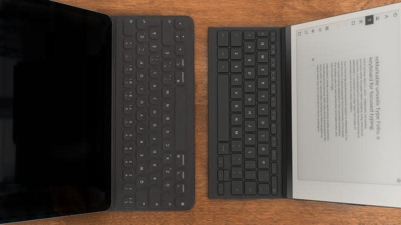 A reMarkable 2 e-note with the Type Folio case deployed sitting next to an iPad Pro with an older Apple keyboard case attached, both sitting on a wooden table.