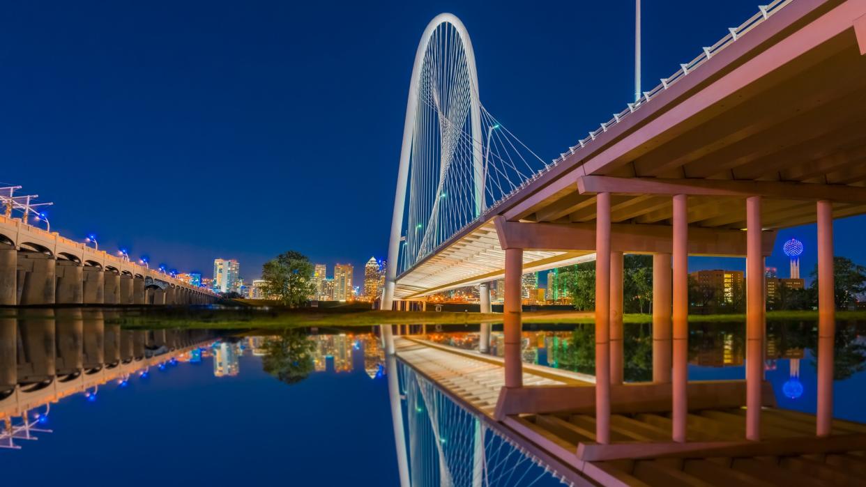 Night lights fill the sky and reflect in the water under the bridge in Dallas, Texas.