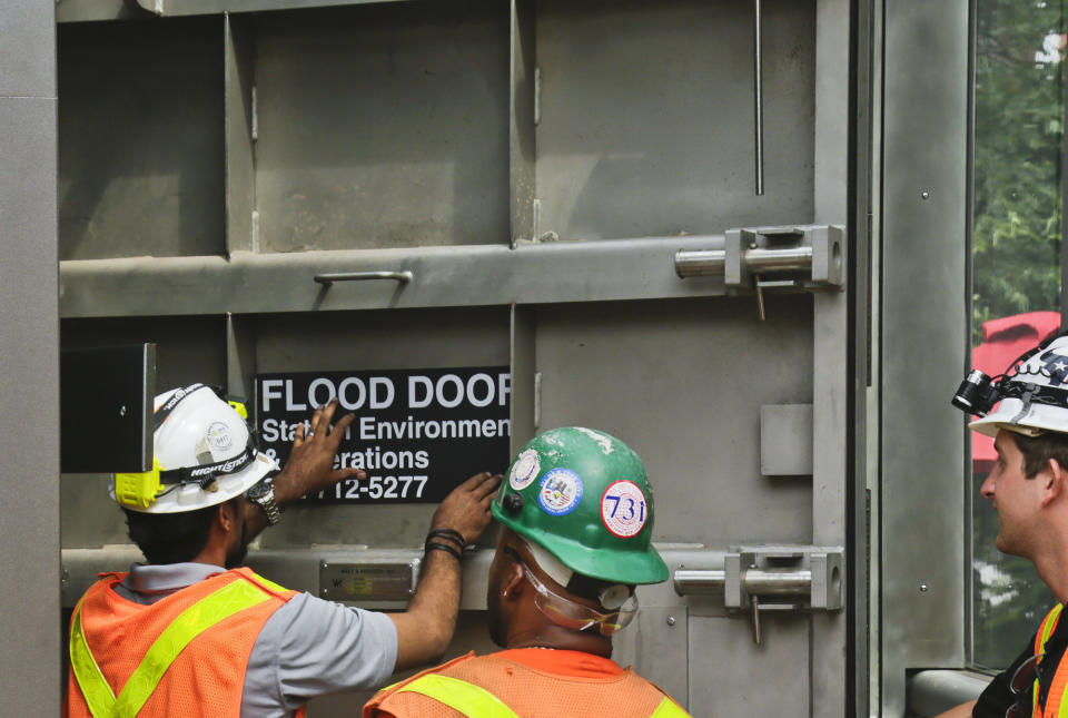 FILE - New York subway workers place a "flood door" decal onto steel doors, installed nearly five years after Superstorm Sandy flooding at South Ferry subway station, in New York on Tuesday June 27, 2017. As weather becomes more extreme and unpredictable caused by climate change, transit officials say that more needs to be done to prepare the East Coast's vital transit systems. (AP Photo/Bebeto Matthews, File)