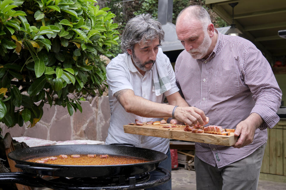 En esta imagen proporcionada por Discovery, José Andrés sostiene una charola con torrezno preparado en una paellera mientras Diego Guerrero lo coloca en una escena de la serie de Discovery + "Jose Andres and Family in Spain" (“Chef José Andrés y familia”). (Xaume Olleros/Discovery vía AP)