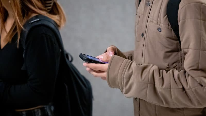 A student uses their phone while walking between classes at Cyprus High School in Magna on Jan. 27, 2023. 