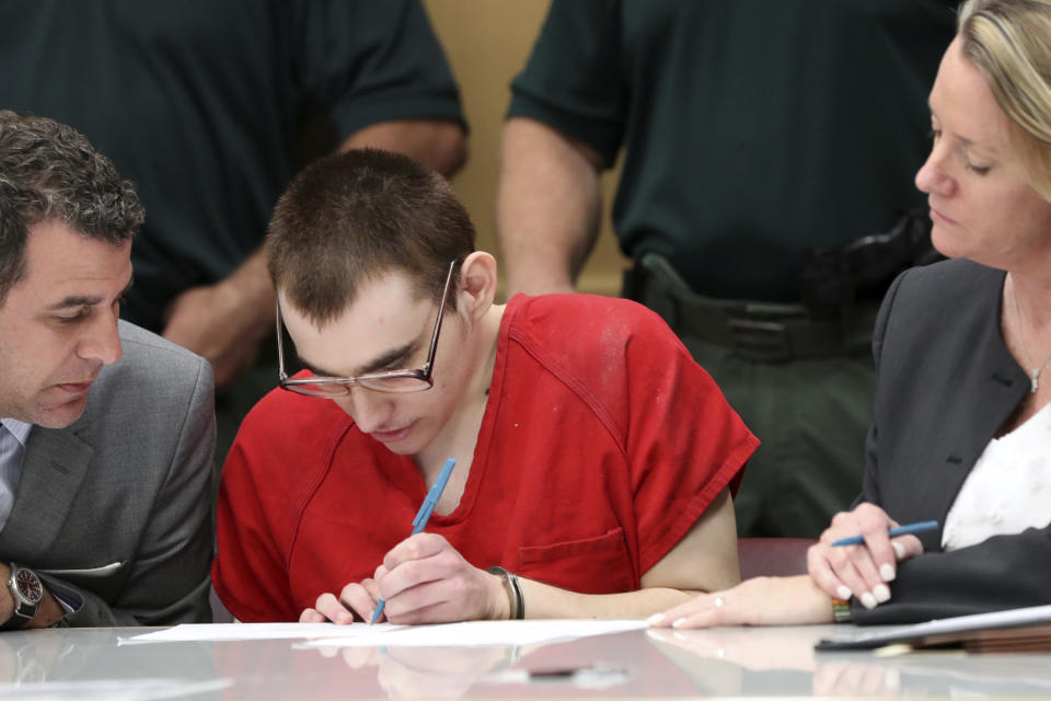 Florida school shooting defendant Nikolas Cruz, sitting between defense attorneys Gabe Ermine and Melisa McNeill, signs a document while handcuffed as a hearing begins at the Broward Courthouse Tuesday, Dec. 10, 2019, in Fort Lauderdale, Fla. (Amy Beth Bennett/South Florida Sun-Sentinel via AP, Pool)